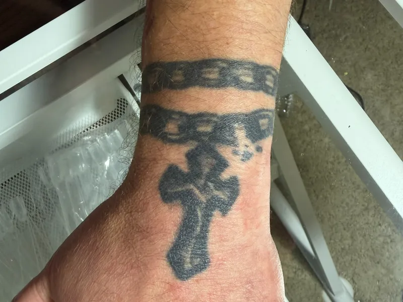 Andrew's left-hand tattoo — a cross with a broken chain, representing breaking the cycle